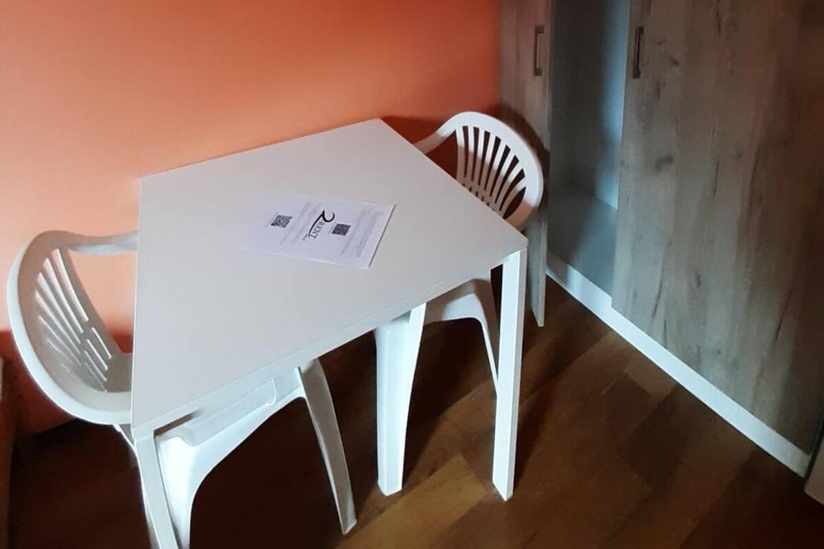 Een kamer met een witte tafel en twee witte stoelen, een garderobe en een oranje wand.