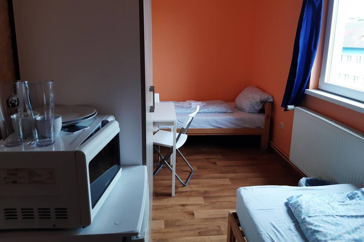 Una habitación pequeña con una cama, un escritorio con computadora y una ventana con cortinas.