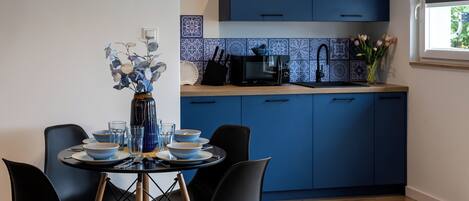 A modern kitchen with blue cabinets, a microwave, and a dining area with a table set for four.