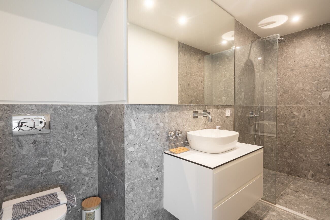 Une salle de bain moderne avec une douche en marbre, un lavabo blanc et une douche à parois de verre.