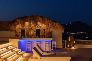 A rooftop bar with a thatched roof, stone walls, and blue ambient lighting.