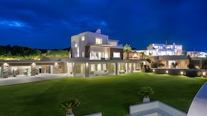 A modern multi-story house with a well-maintained lawn and outdoor seating area. - Alegria Mykonos 10 Suites – Luxury Estate with 14 Suites and Panoramic Sea Views (Kalafatis)