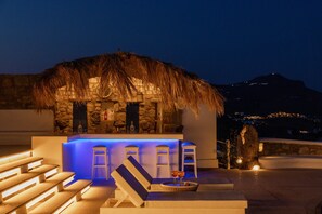 A rooftop bar with a thatched roof, stone walls, and blue ambient lighting.