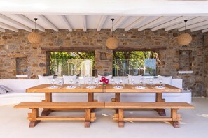 An outdoor dining area with stone walls, white furniture, and wooden tables.