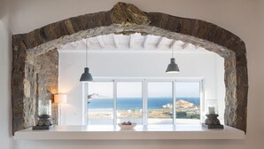 A room with a stone arch, a white counter, two pendant lights, and a view of the sea. - Alegria Mykonos 10 Suites – Luxury Estate with 14 Suites and Panoramic Sea Views (Kalafatis)