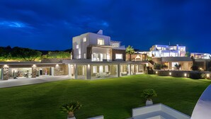 Una casa moderna de varios pisos con un césped cuidado y un área de estar al aire libre.