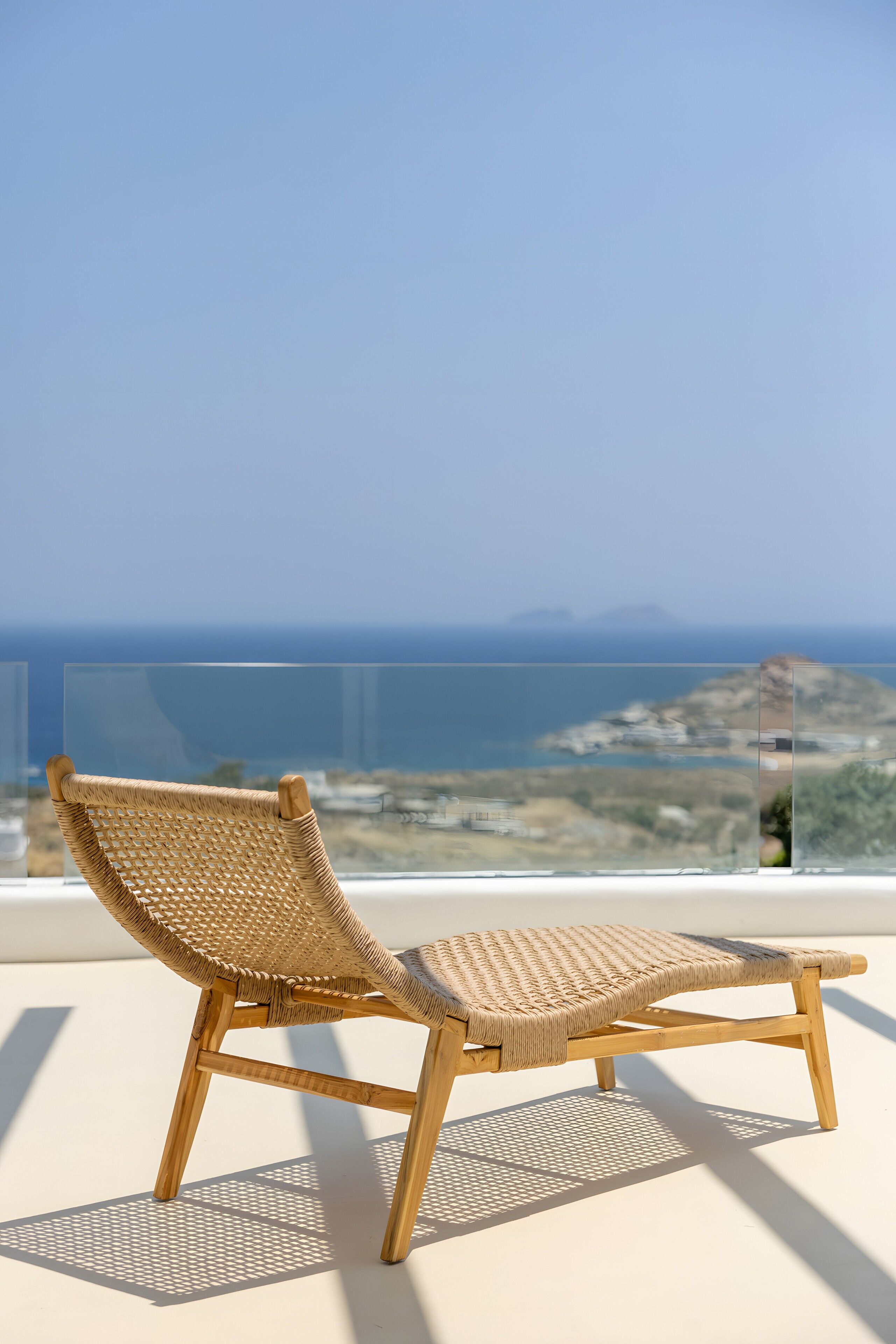 Una silla de mimbre en un balcón con vistas despejadas al mar y a la costa lejana.