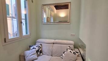 A room with a light-colored sofa, a large mirror, and a window with blinds.