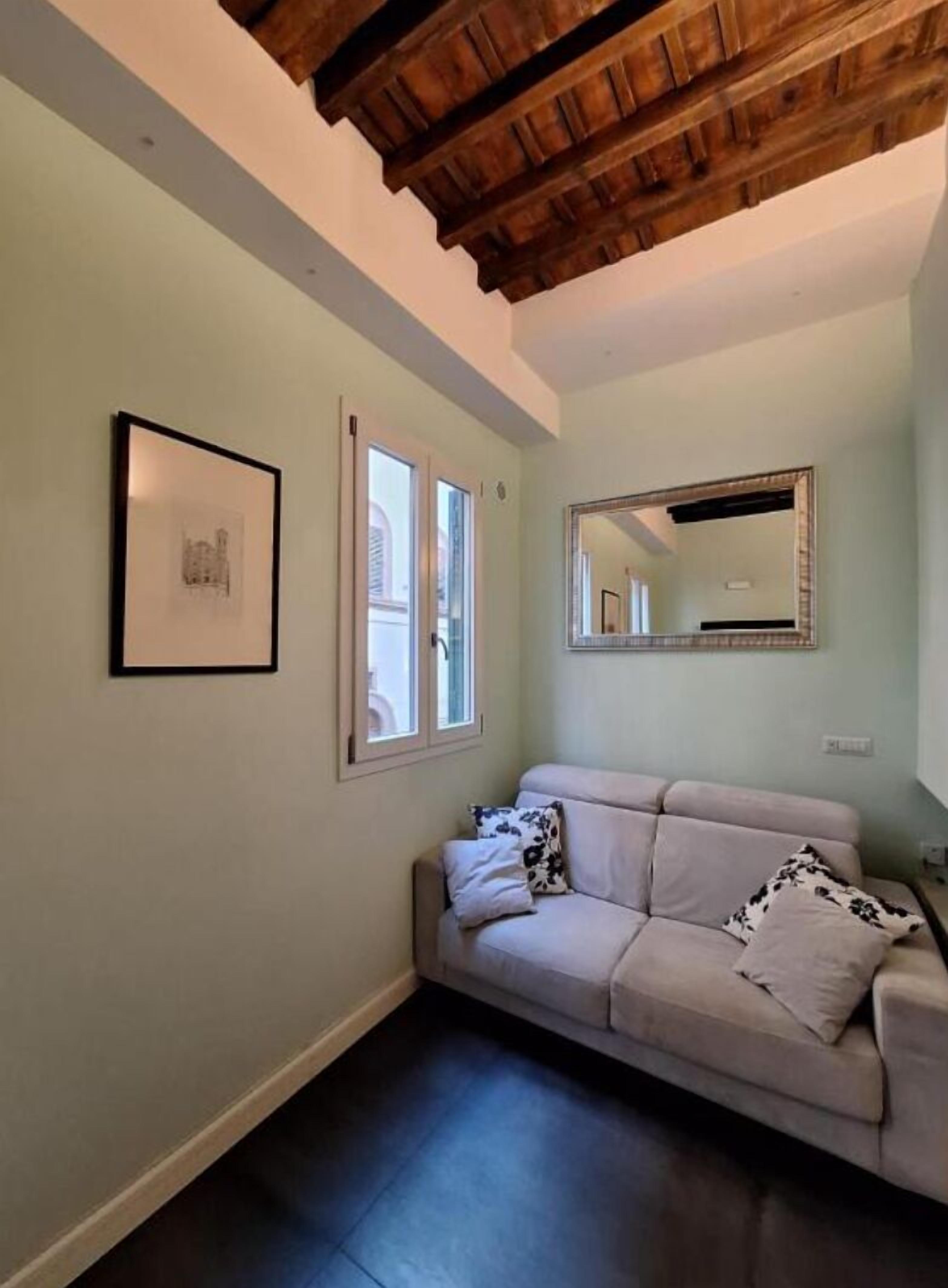 Una habitación con un sofá de color claro, un cuadro en la pared y un espejo grande.