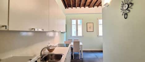 A kitchen with white cabinets, a wooden ceiling, a sink, and a microwave. There is a dining area with a table and chairs in the background.