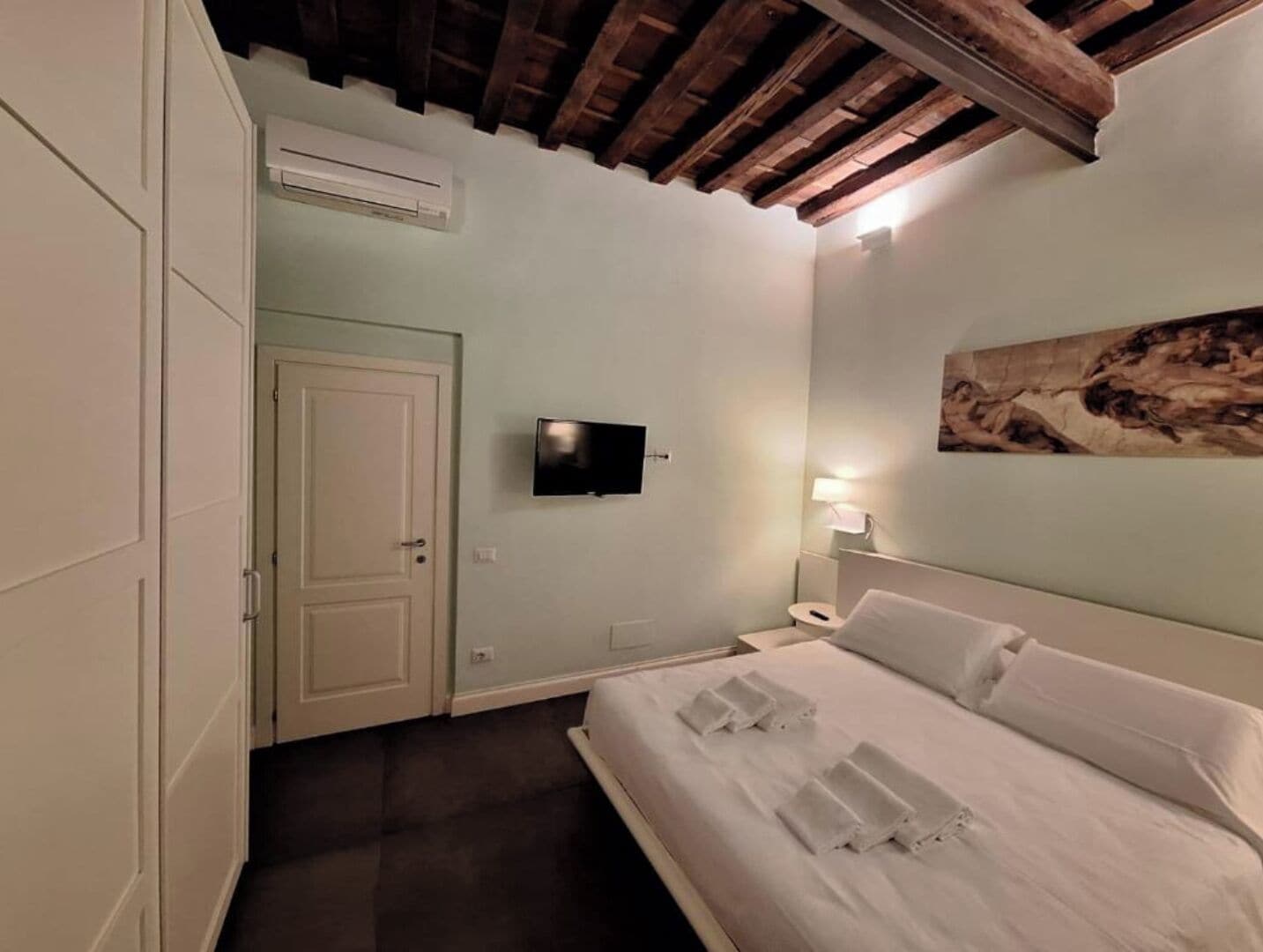 Ein Hotelzimmer mit Bett, Flachbildfernseher, einem Bild an der Wand und einer Klimaanlage.