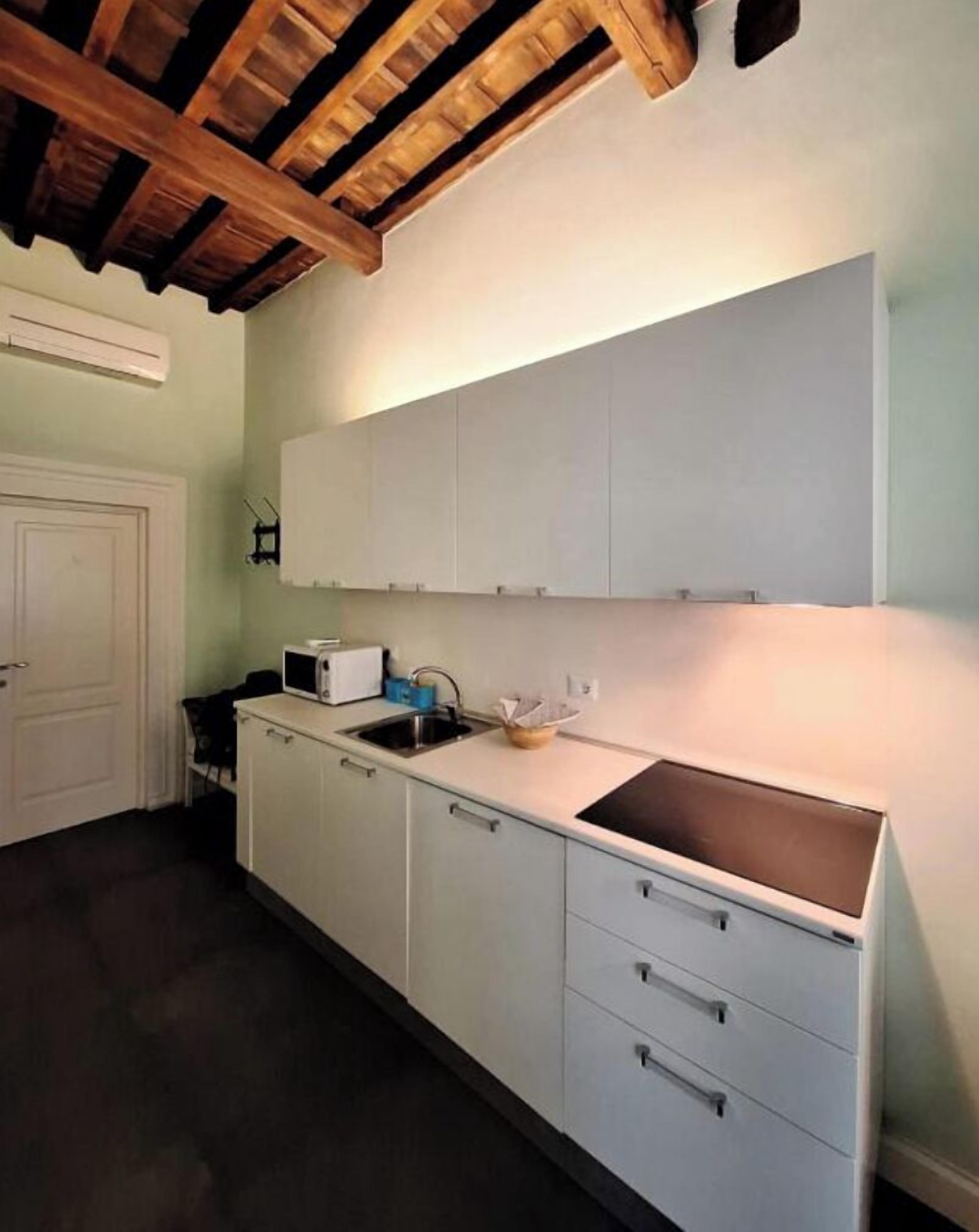 Une cuisine avec des meubles blancs, un plan de travail noir et un plafond en bois.
