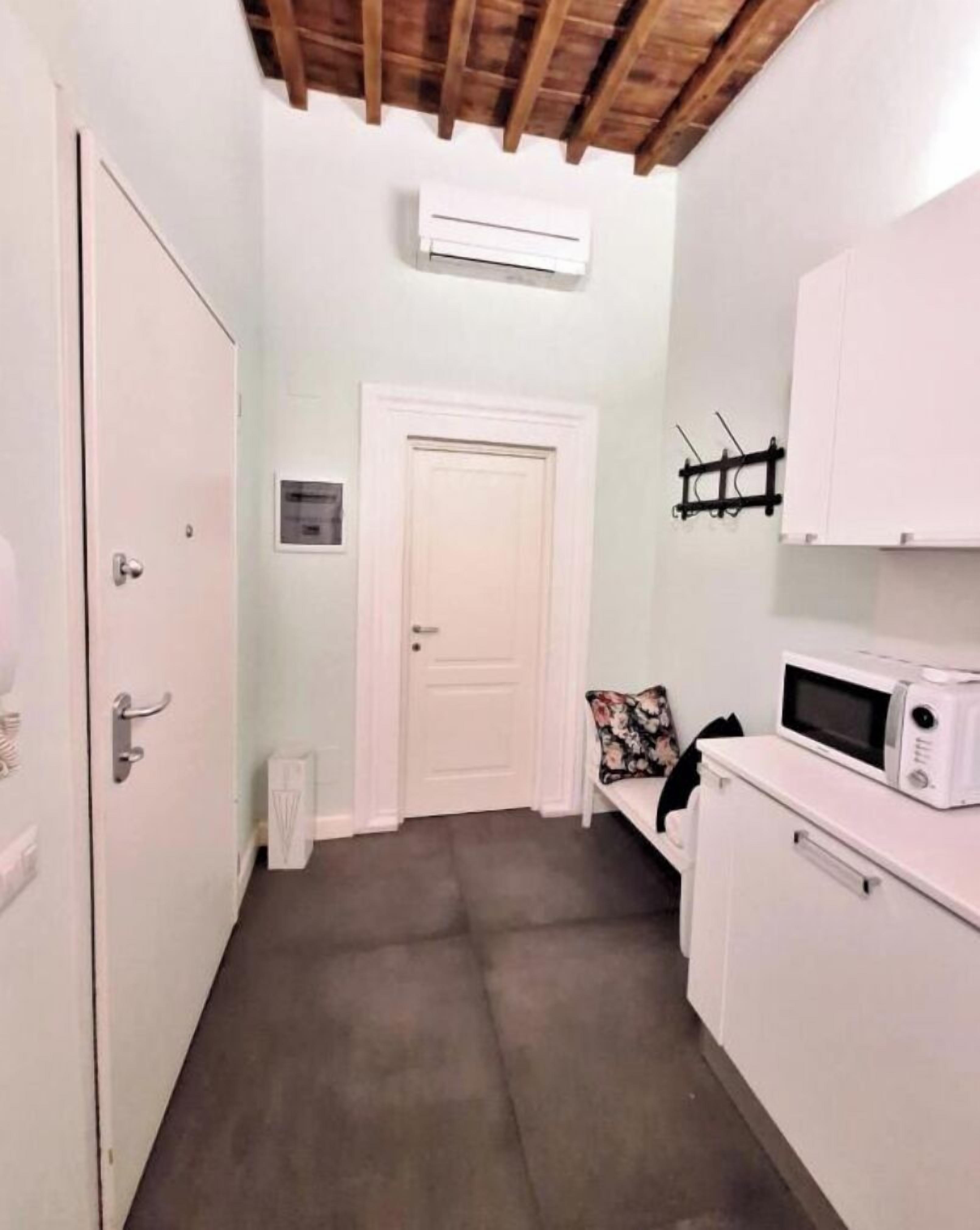 A narrow hallway with a white door, a white cabinet with a microwave, and a ceiling fan.