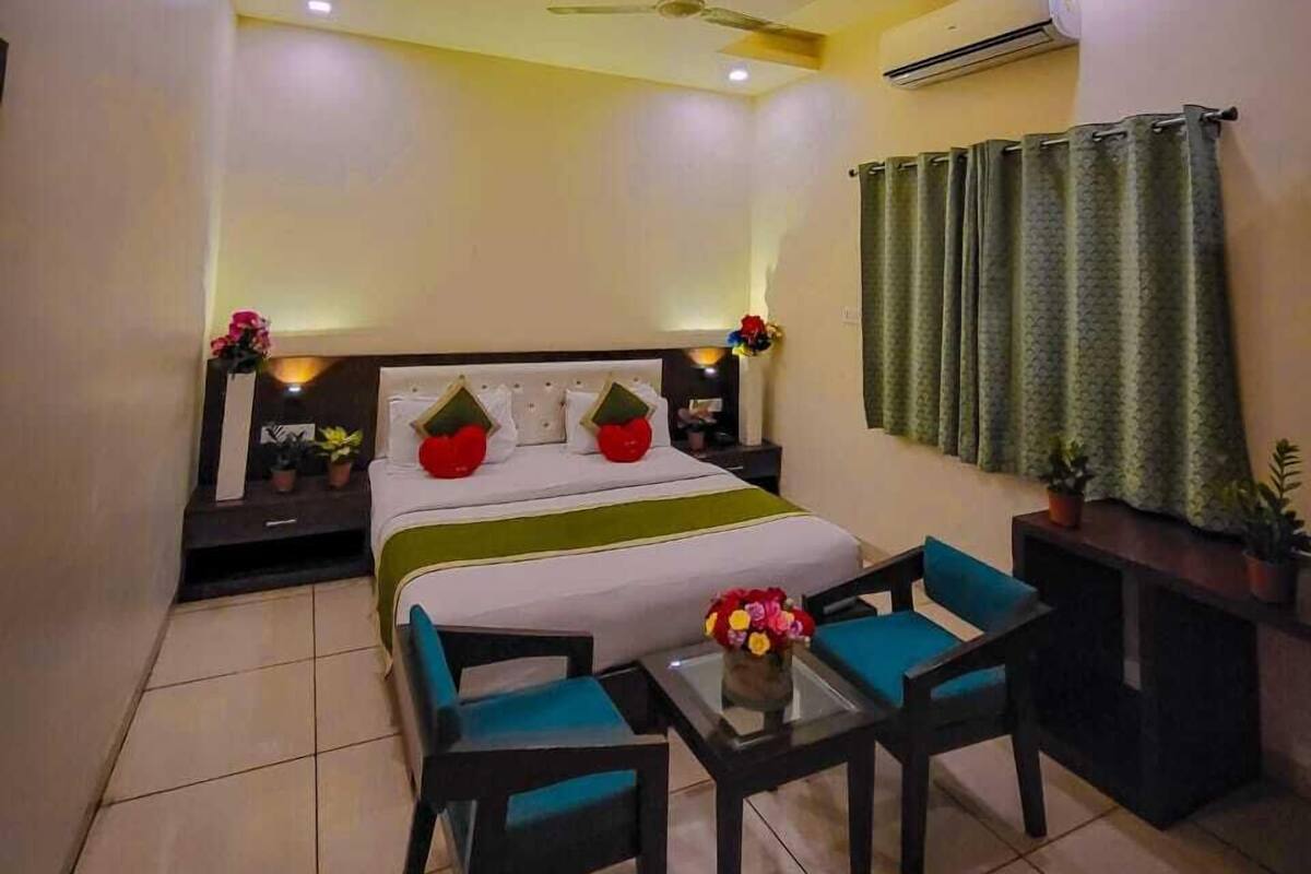 Une chambre d’hôtel comprenant un lit, un bureau, deux chaises, un ventilateur de plafond, un climatiseur et une fenêtre avec des rideaux.