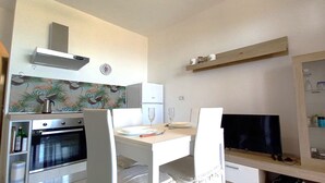 Eine kleine Küche mit Herd, Backofen und Mikrowelle. Ein Esstisch mit Stühlen und ein Flachbildfernseher auf einem Schrank.
