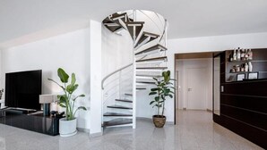 A modern interior with a spiral staircase, a flat-screen TV, and potted plants.