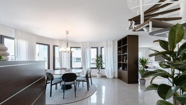 A modern living room with a dining area, a staircase, and a bookshelf.