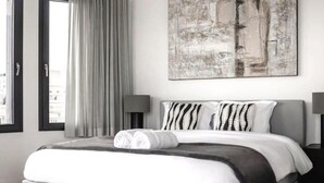 A modern hotel room with a large bed, a view through the window, and a painting on the wall.