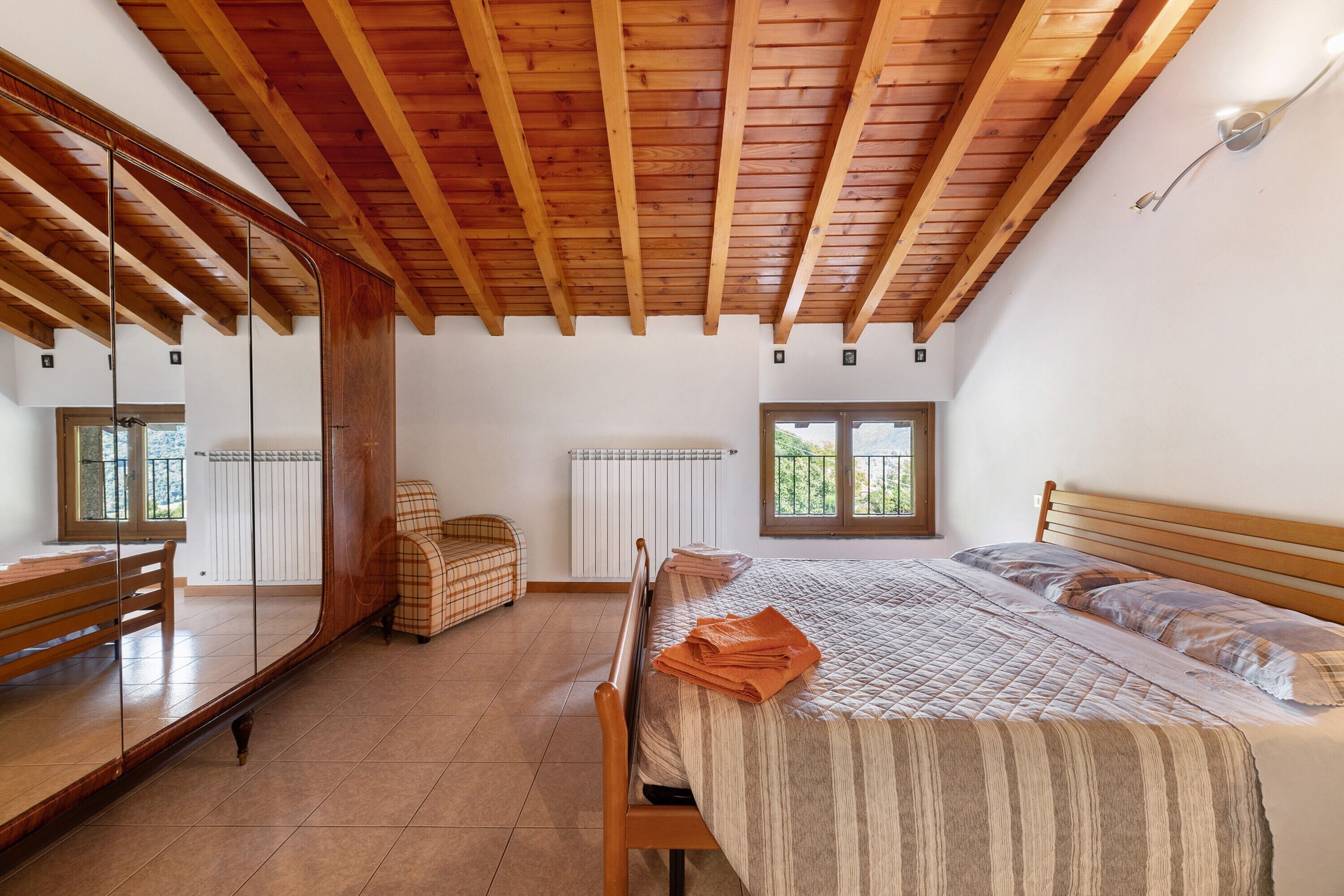 Ein Schlafzimmer mit Holzboden, einem Bett mit gestreifter Bettdecke, einem Stuhl, einem Spiegel und einem Fenster.