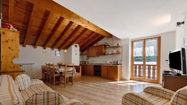 A living room with a sofa, a dining table with chairs, a kitchen area with wooden cabinets, and a balcony with a view. - Holiday Home 'Vendrogno' with Mountain View, Private Garden and Wi-Fi (Bellano)