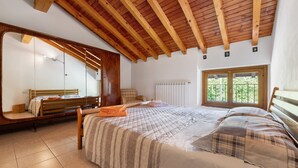 A bedroom with a wooden ceiling, a large bed with a quilted bedspread, a wooden bench, a mirror, and a window with a view. - Holiday Home 'Vendrogno' with Mountain View, Private Garden and Wi-Fi (Bellano)