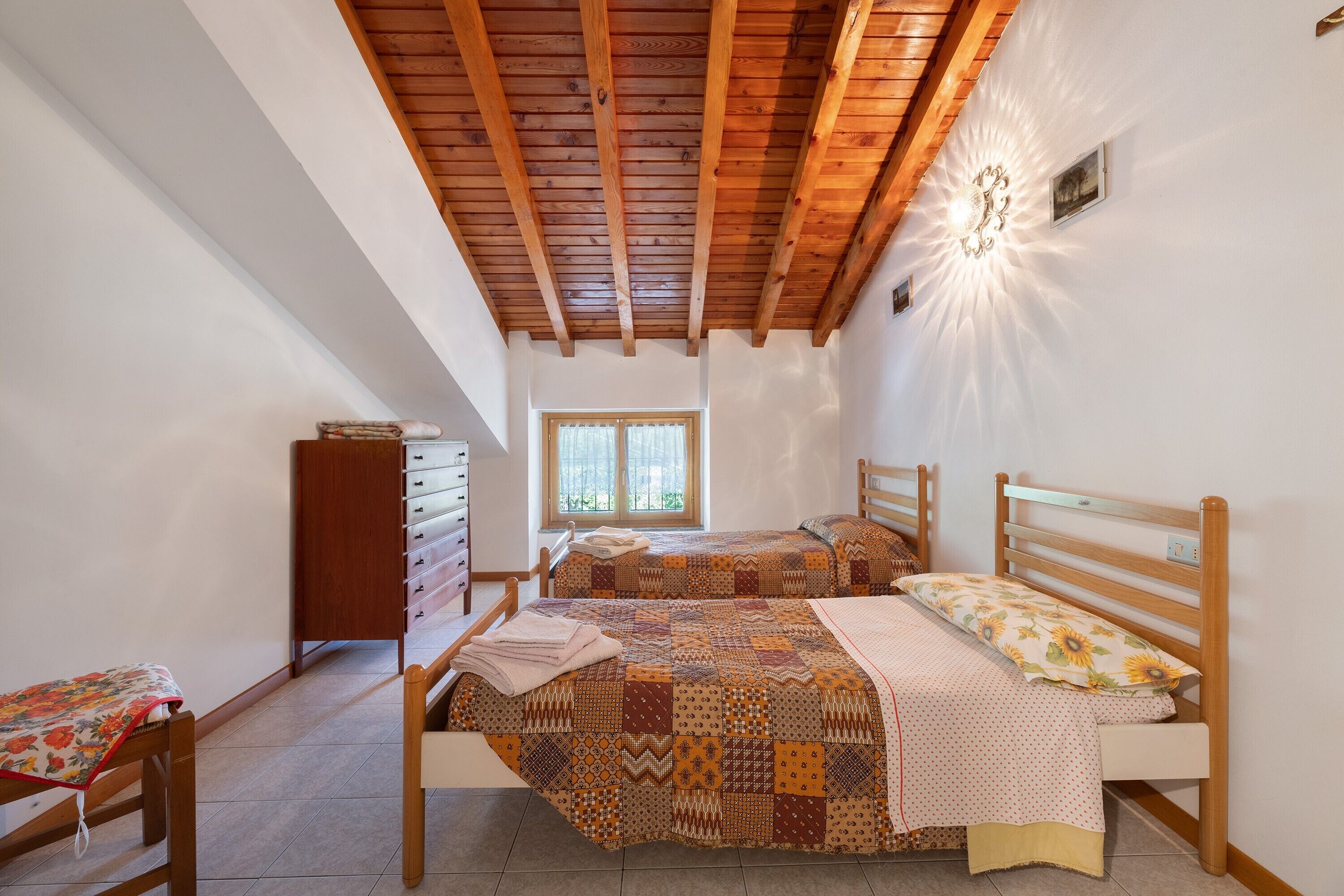 Ein Schlafzimmer mit zwei Betten, Holzbalken an der Decke, einem Fenster und einem Schminktisch.