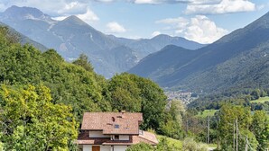 A house with a tiled roof, surrounded by lush greenery and mountains in the background. - Holiday Home 'Vendrogno' with Mountain View, Private Garden and Wi-Fi (Bellano)