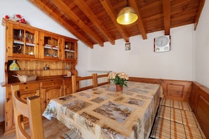 Zona pranzo con mobili in legno, tovaglia trapuntata e orologio appeso al muro.