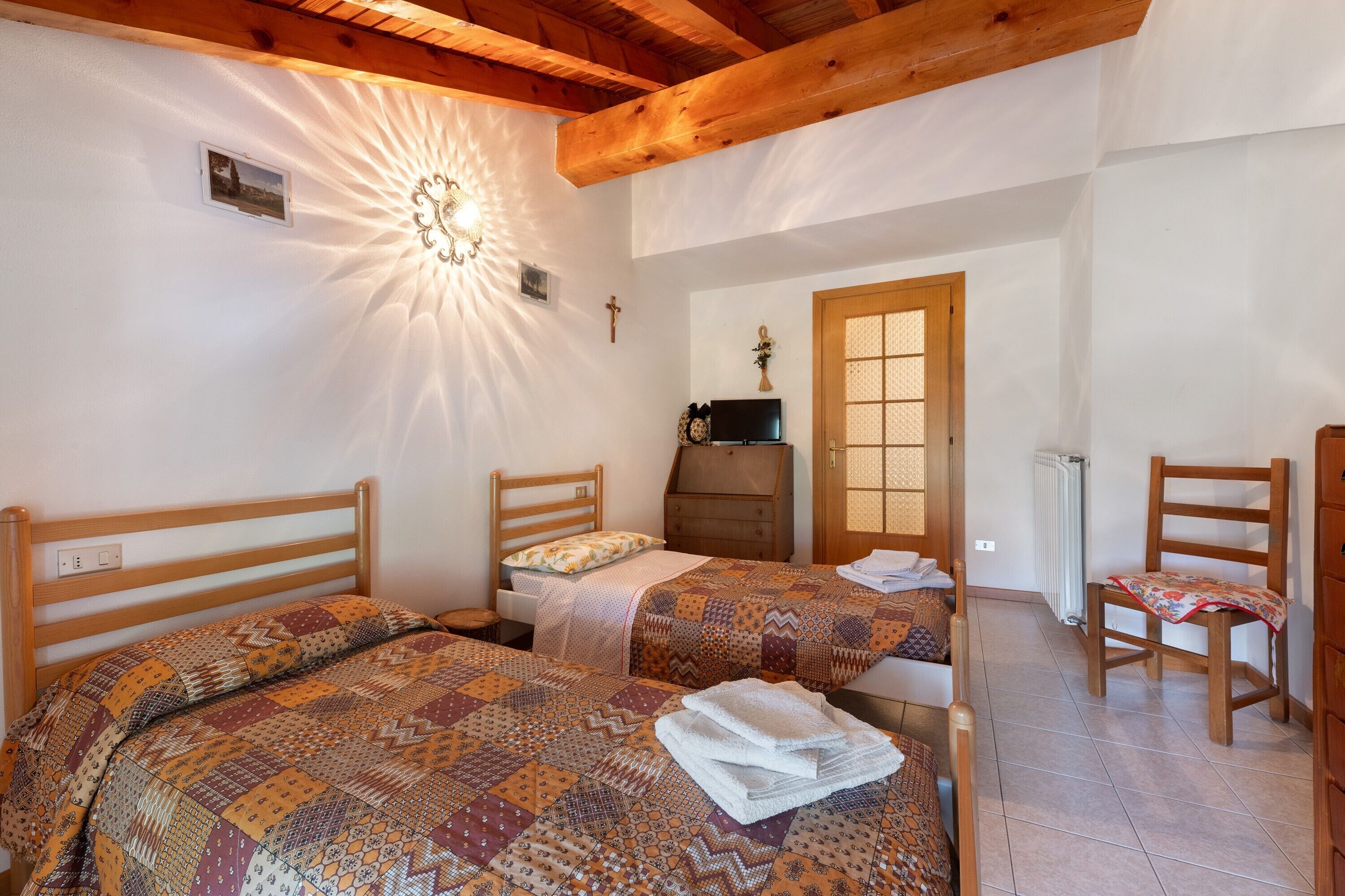 A bedroom with two beds, a wooden ceiling, a radiator, and a wooden chair.