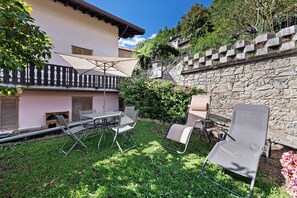 A patio with outdoor furniture, a stone wall, and a pink building with shutters. - Holiday Home 'Vendrogno' with Mountain View, Private Garden and Wi-Fi (Bellano)