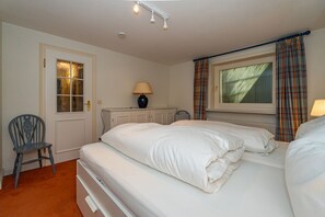 A bedroom with two beds, a chair, a lamp, a radiator, and a window with curtains. - House Daanshoog - House Daanshoog on Sylt - Comfortable vacation home with sauna, (Sylt)