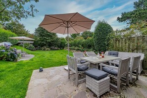 An outdoor patio with a table and chairs, a large umbrella, and a stone pathway. - House Daanshoog - House Daanshoog on Sylt - Comfortable vacation home with sauna, (Sylt)