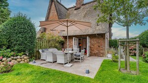 Una casa con techo de paja, un patio con muebles de exterior y un jardín.