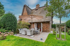 A house with a thatched roof, a patio with outdoor furniture, and a garden. - House Daanshoog - House Daanshoog on Sylt - Comfortable vacation home with sauna, (Sylt)