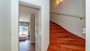 Un pasillo que conduce a un dormitorio con cortina a rayas, una escalera con alfombra naranja y una puerta blanca.