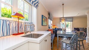 Una cocina con encimera blanca, un fregadero y una zona de comedor con mesa y sillas.