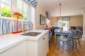A kitchen with a white countertop, a sink, and a dining area with a table and chairs. - House Daanshoog - House Daanshoog on Sylt - Comfortable vacation home with sauna, (Sylt)