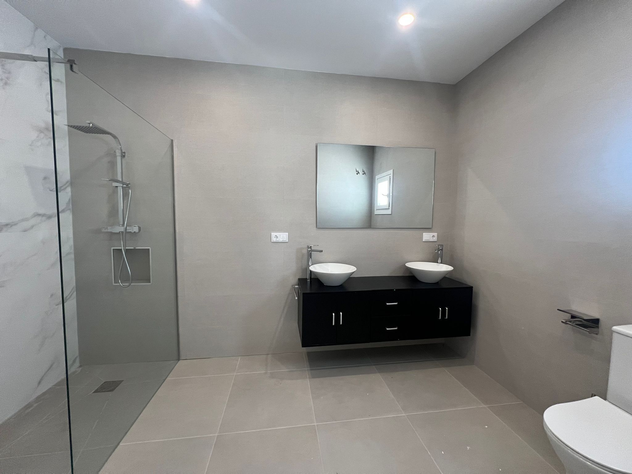 Une salle de bain moderne avec une douche à parois de verre, deux lavabos, un grand miroir et des toilettes.