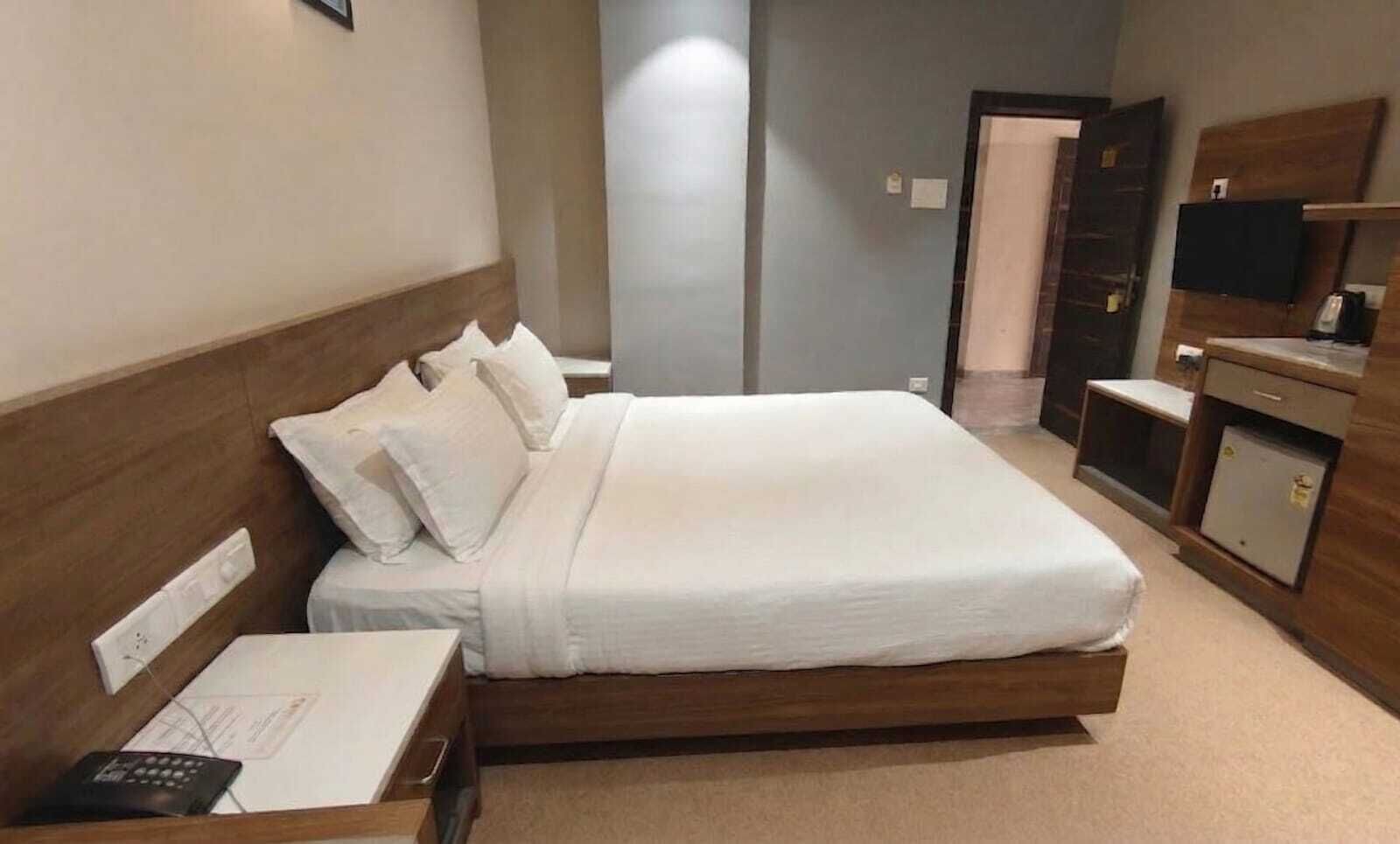 Quarto de hotel com cama, mesa de cabeceira, escrivaninha, cadeira, televisão e guarda-roupa.