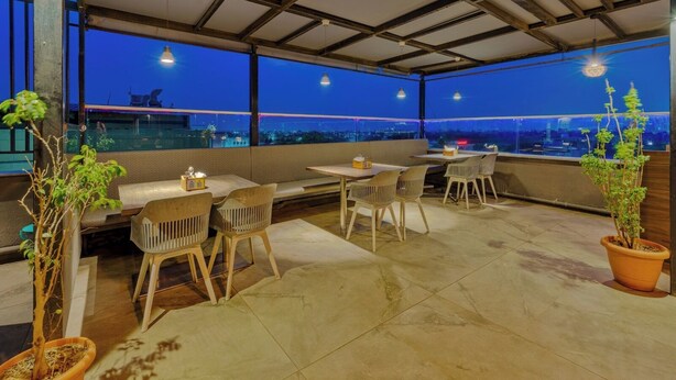 A rooftop terrace with seating and tables, large windows offering a city view, and potted plants. - O'Nest Pearl (Miraj)