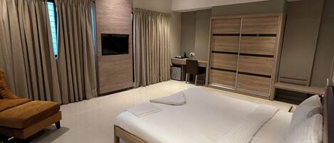 A modern hotel room with a bed, a desk, a chair, a TV, and a ceiling fan.