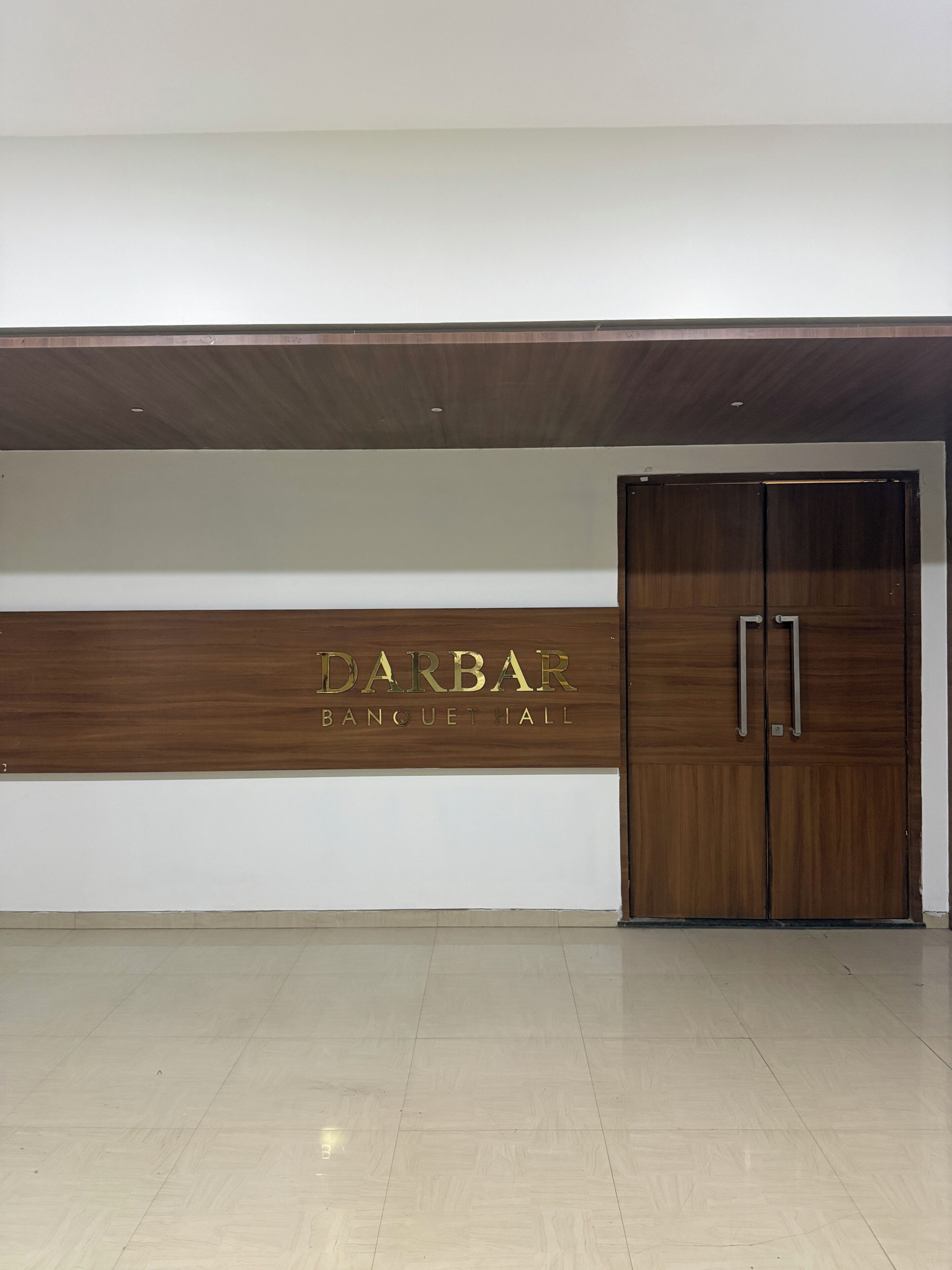 Entrada d'hotel amb taulell de recepció de fusta i una porta gran.