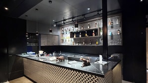 A modern bar area with a counter, shelves of bottles, and a patterned wall. - O'Nest Pearl (Miraj)