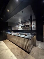 Un área de bar moderna con mostrador, estantes llenos de botellas y pared decorada.