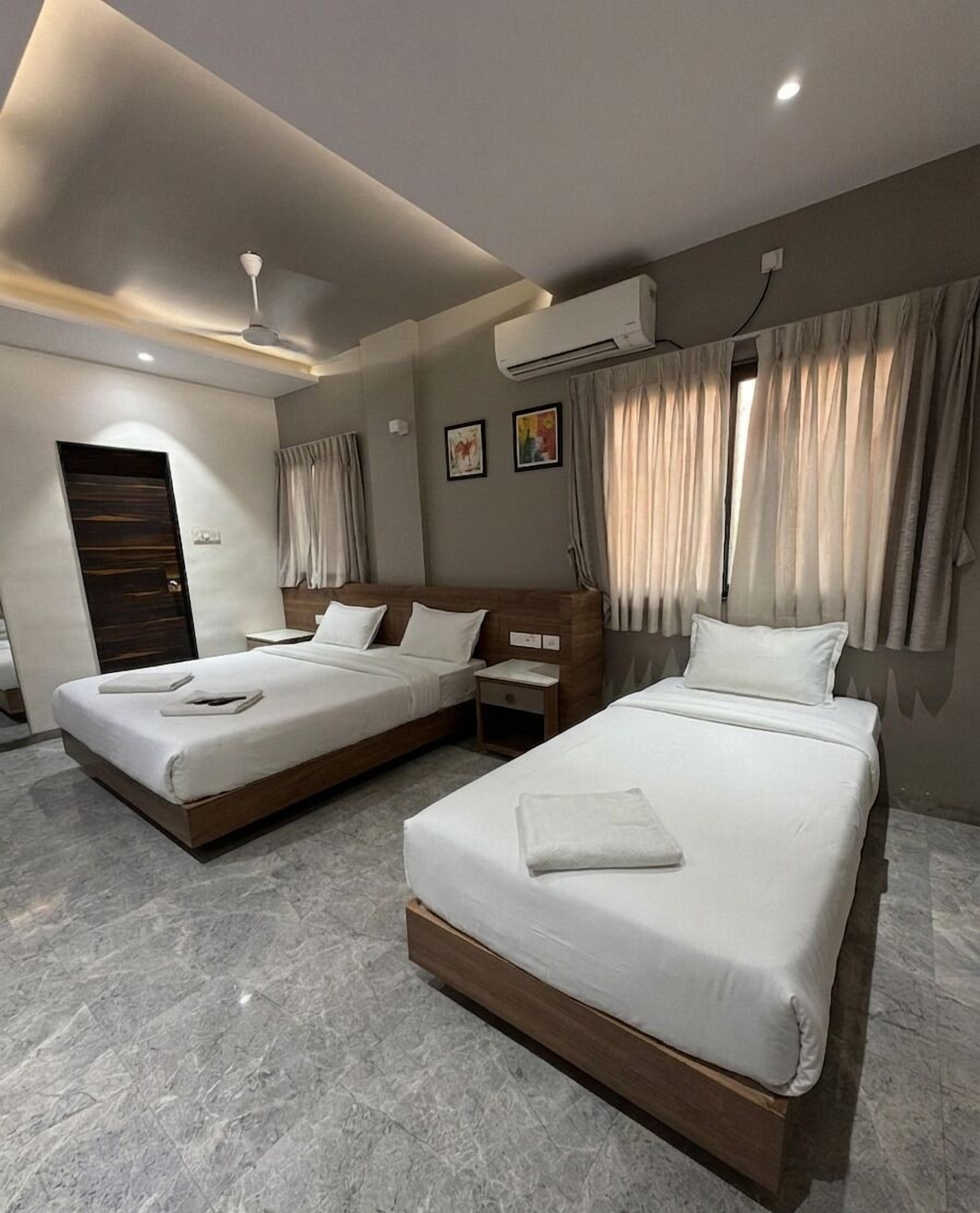 A hotel room with two beds, a wooden headboard, a nightstand, an air conditioning unit, and a door.