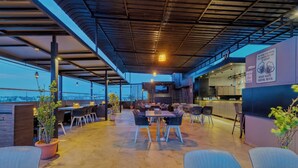 An outdoor dining area with tables and chairs, a bar area, and a city view. - O'Nest Pearl (Miraj)
