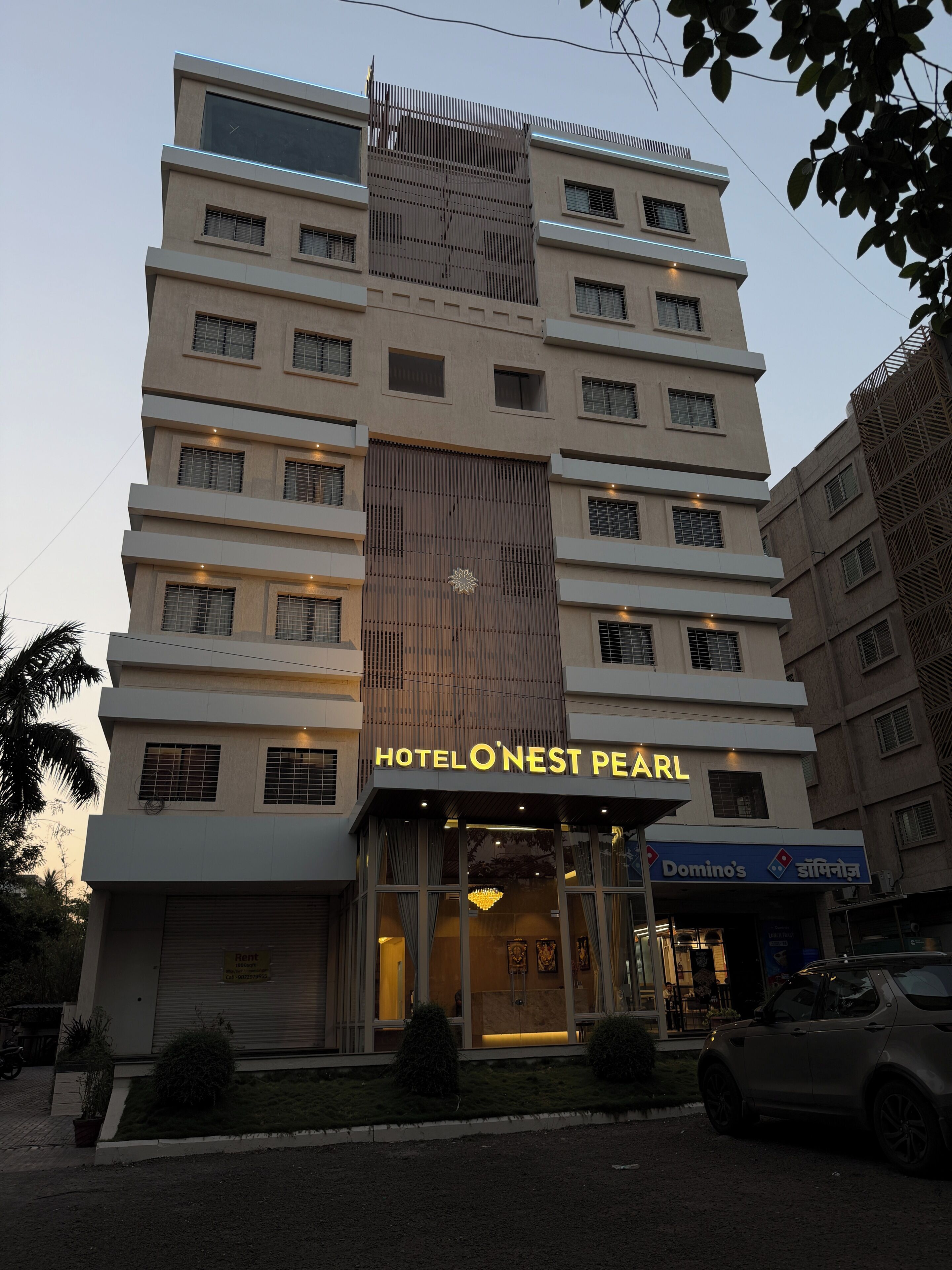 A multi-story hotel named 'HOTEL O'NEST PEARL' with a modern facade, large windows, and a visible Domino's Pizza sign.