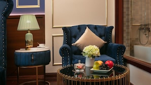 Una poltrona blu con un cuscino beige, un tavolino rotondo con una lampada e un cesto di frutta su un tavolino da caffè.