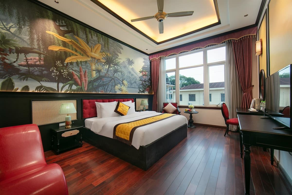 Habitación de hotel con una cama grande, un escritorio, una silla, un televisor y una ventana con cortinas.