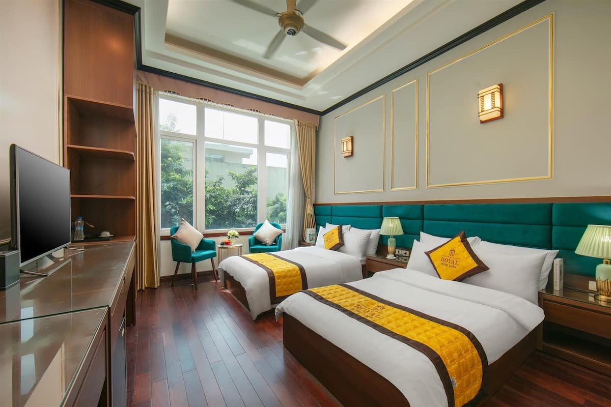 Habitación de hotel con dos camas, televisión y vistas al exterior con zonas verdes.